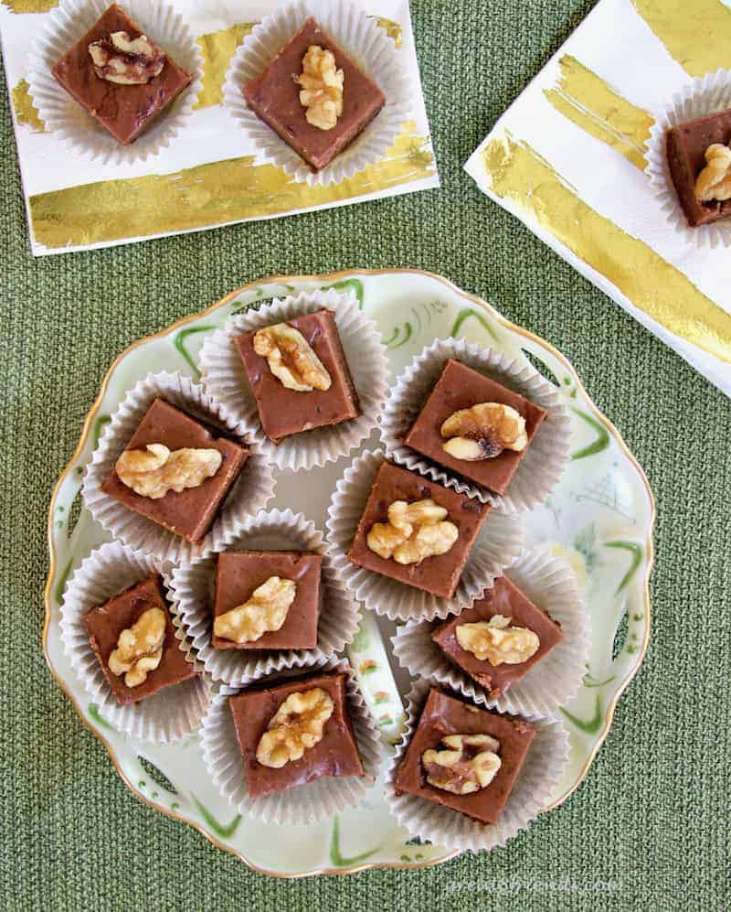 Overhead shot of a round plate containing pieces of walnut topped fudge on a green background.