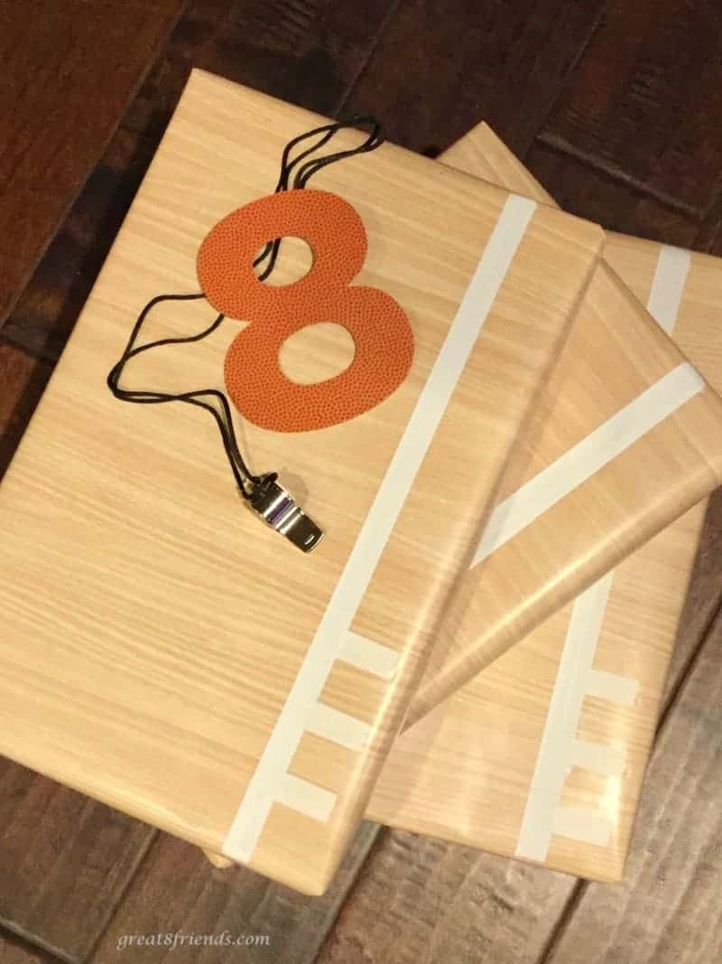 Three gifts wrapped in wood looking paper with masking tape lines (to look like a basketball court) with a cut out 8 and a whistle.