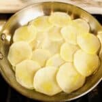 Process shot of a layer of thinly sliced potatoes topped with melted butter in a frying pan.