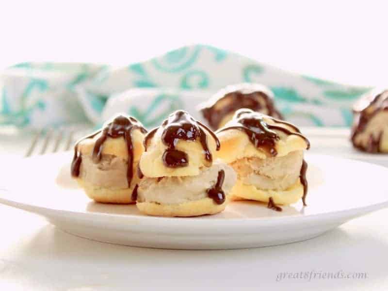 Three Profiteroles cut in half with coffee ice cream and chocolate sauce on a white plate.