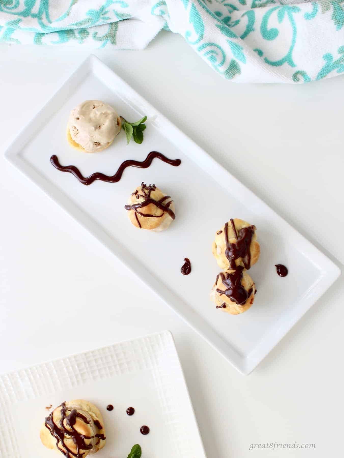 Profiteroles with coffee ice cream and chocolate sauce on a white rectangular plate.