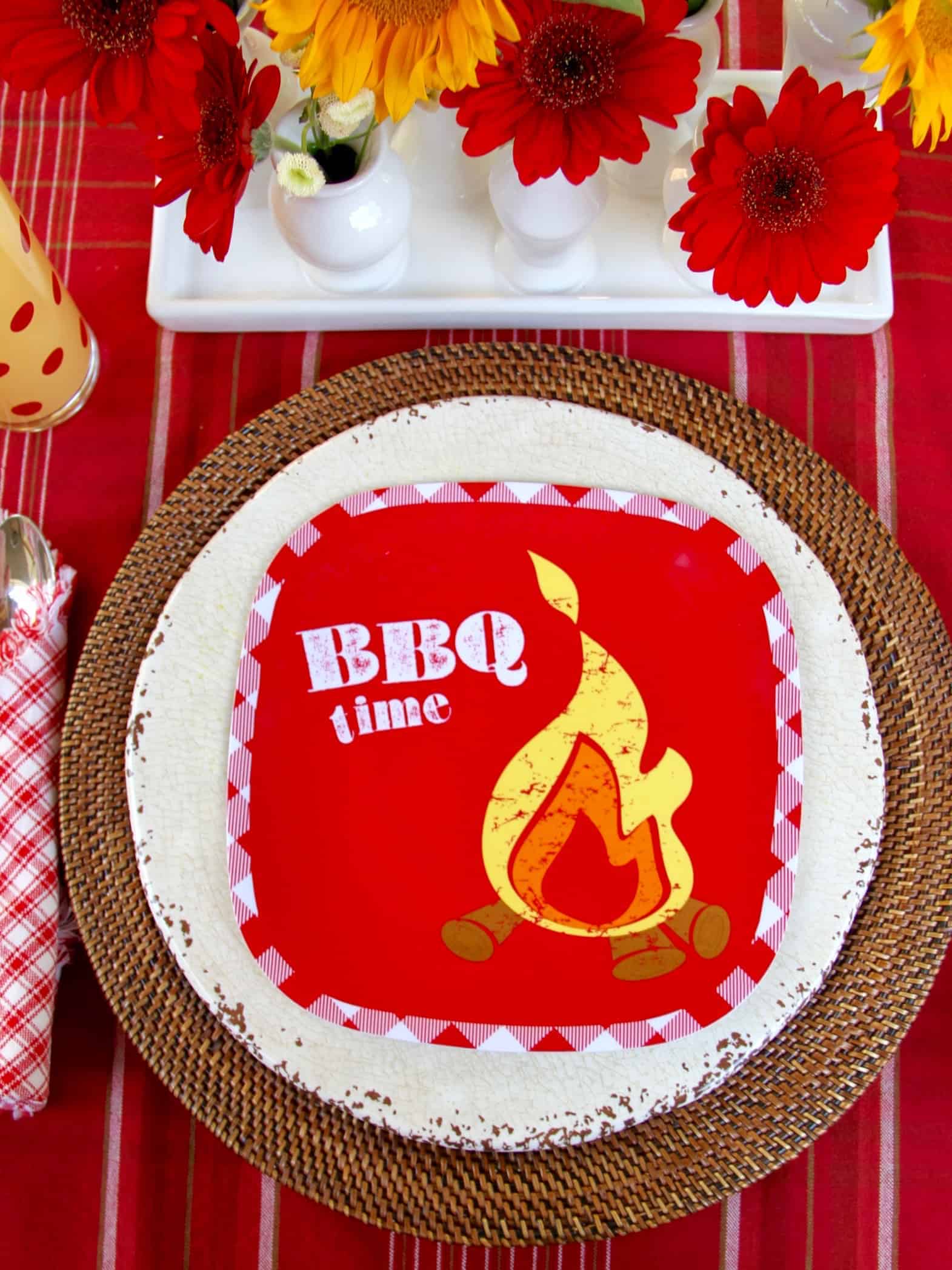 A place setting at a backyard barbecue using a bright red plate that says BBQ time on it.