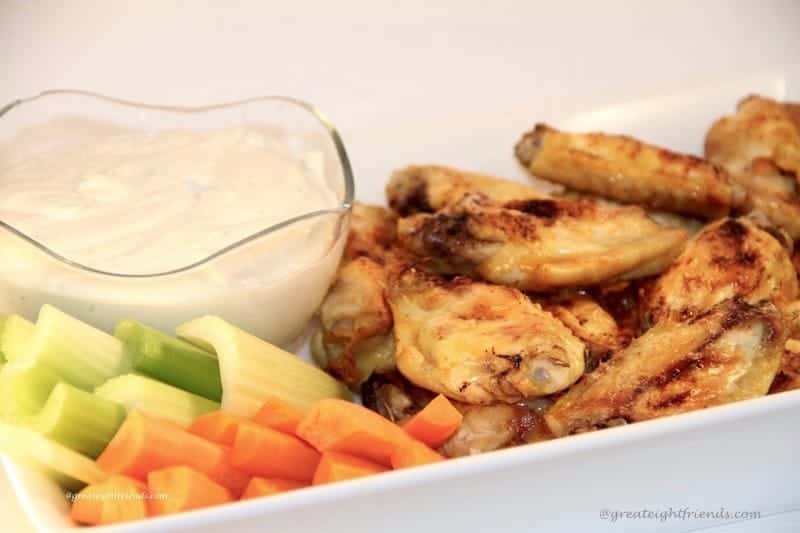 Chicken wings, carrot and celery sticks with a white dip in a white oblong serving dish.