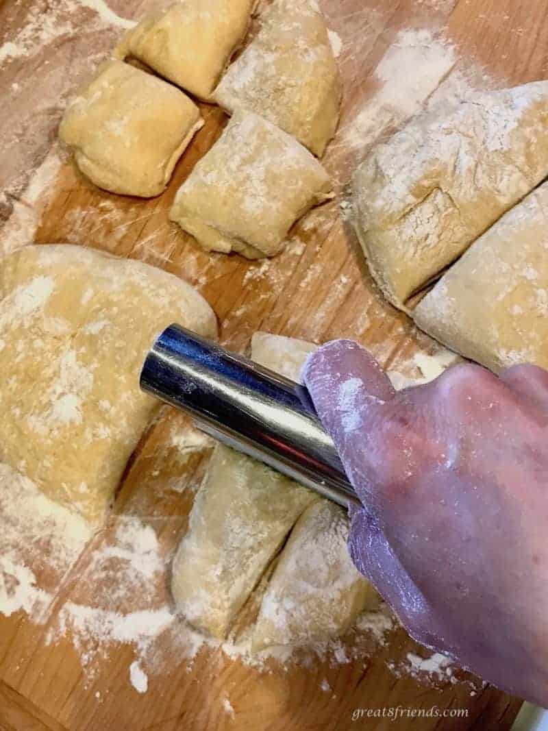 Hawaiian Bread dough being cut with a dough scraper into smaller rolls on a wood board covered with flour.