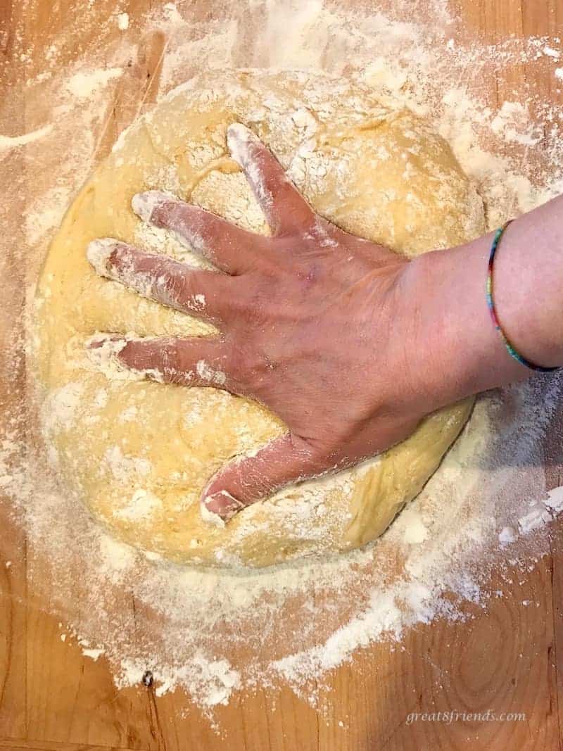 Hawaiian Bread dough being flattened with the palm of a hand on a wooden board covered with flour.
