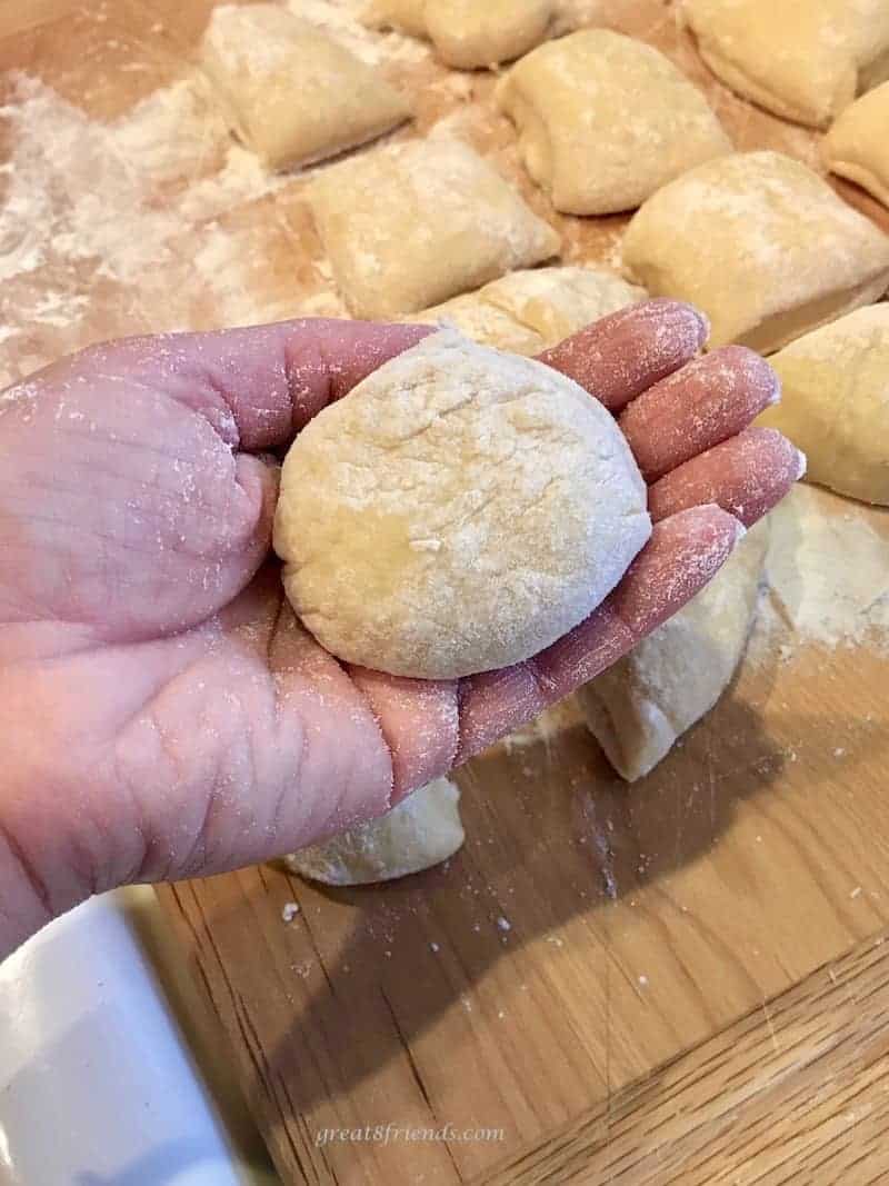 A Hawaiian roll being held in a hand with several other cut rolls on a wood board.