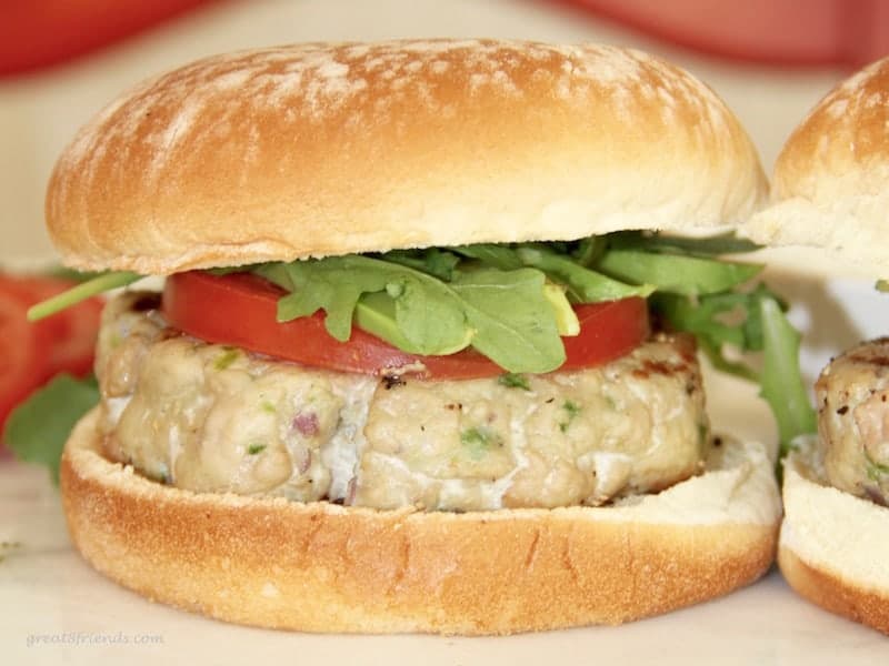 An unclose shot of a tuna burger on a bun with a slice of tomato and arugula.