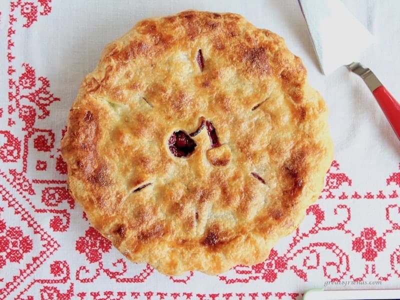 Overhead shot of baked Cherry Pie on a red and white embroidered tablecloth.