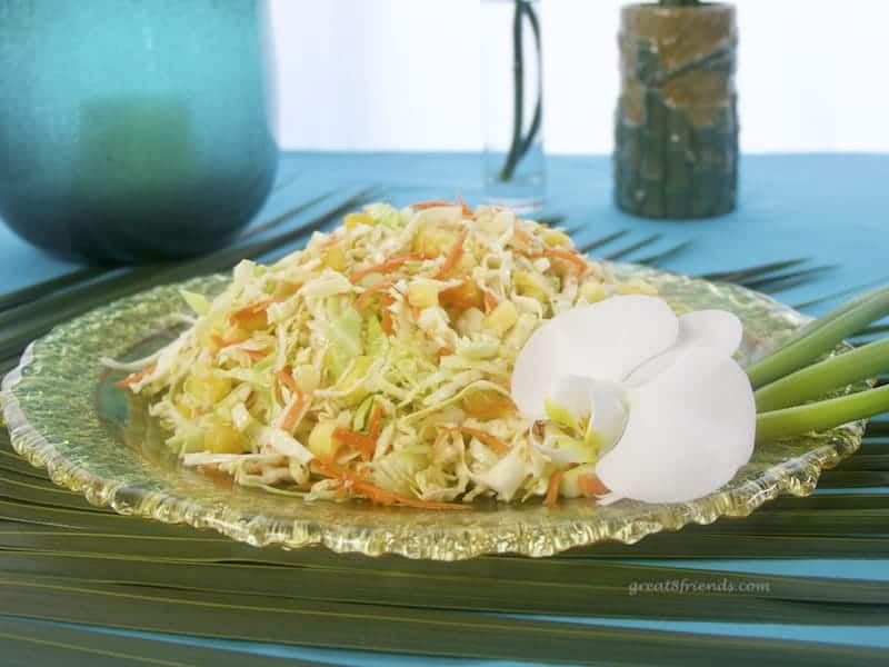 A round platter of Pineapple Sesame Slaw garnished with an orchid sitting on a palm leaf.