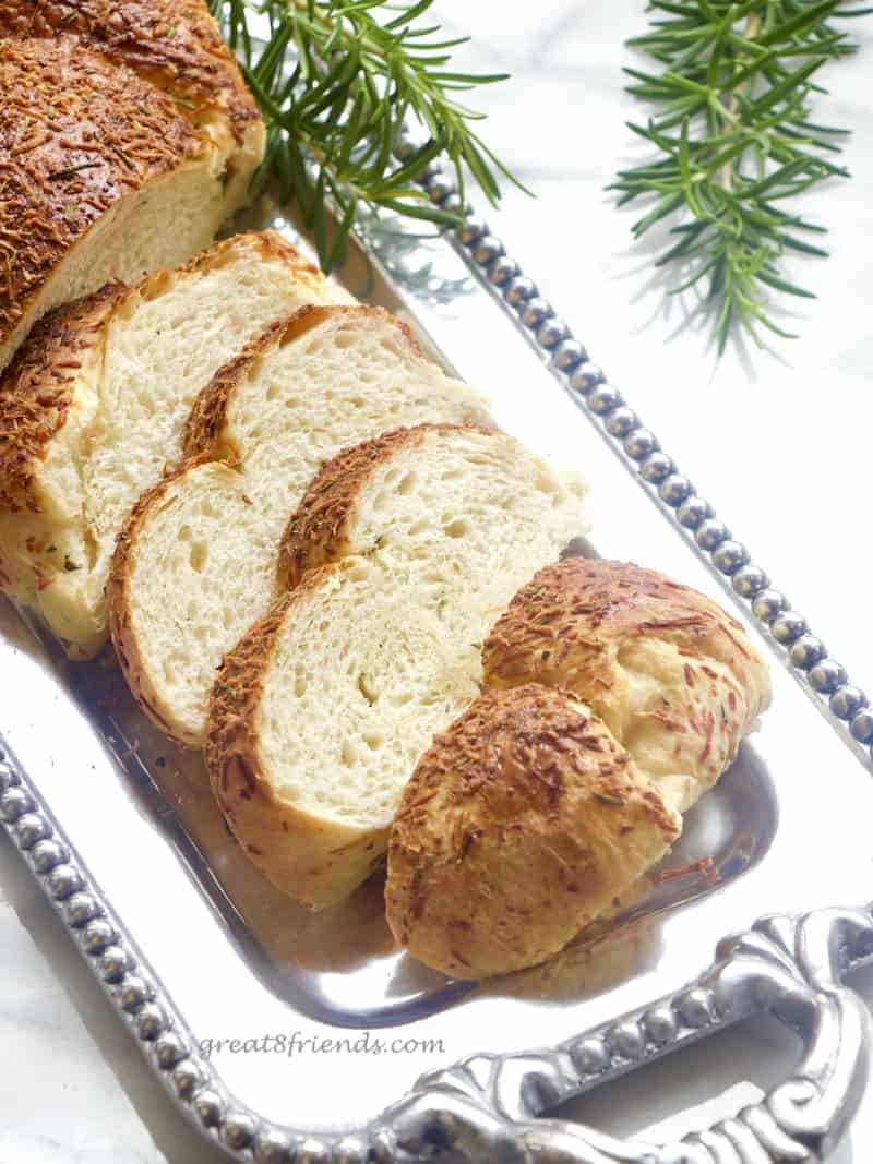 Slices of bread on a silver tray with some rosemary laying around.