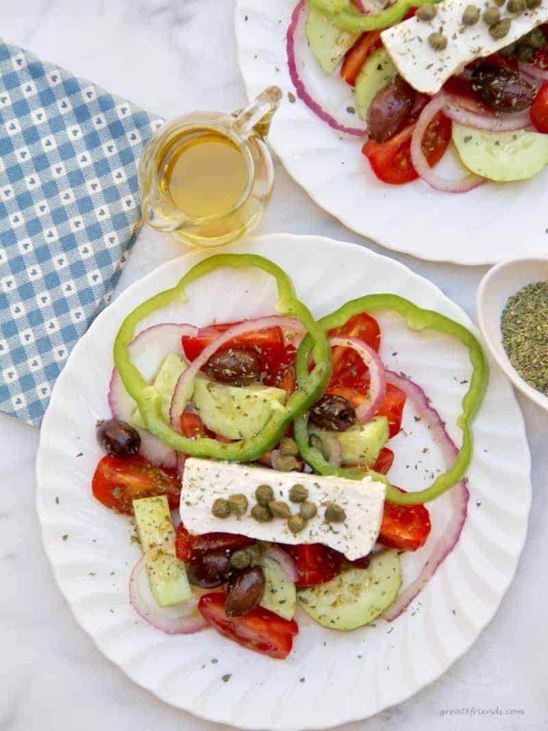 Overhead view of two Greek Salad plates with small pitcher of olive oil  and oregano on the side.