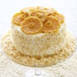 Pineapple Rum Cake with sides covered with toasted coconut and topped with round slices of candied pineapple. The cake in on a glass pedestal.