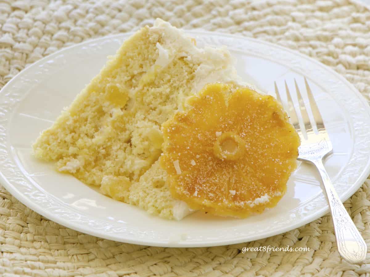 A slice of yellow cake laying on a white plate with a piece of candied pineapple propped against it.
