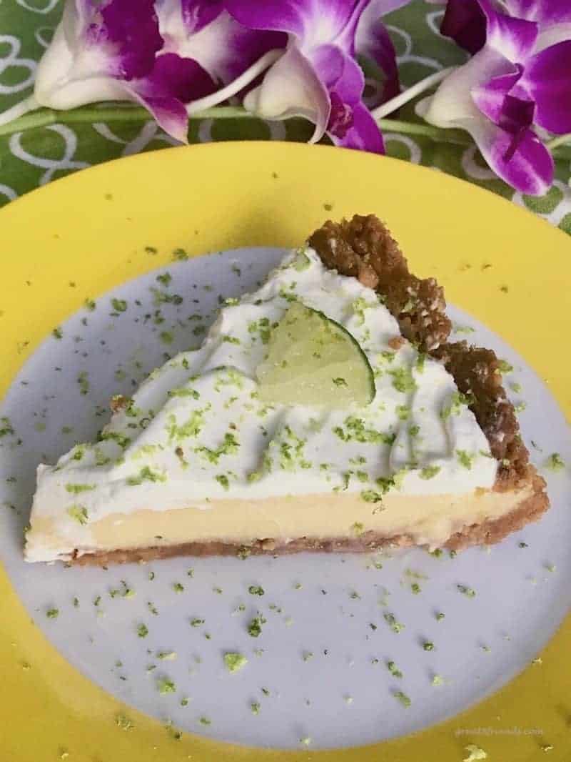 A slice of key lime pie on a white plate with a wide yellow rim with some orchids.