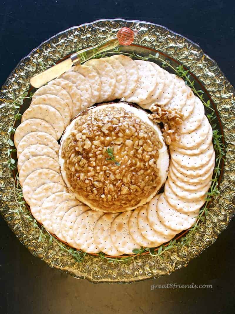 Overhead shot of a round yellow glass platter with a cheese terrine in the middle surrounded by crackers and garnished with thyme.