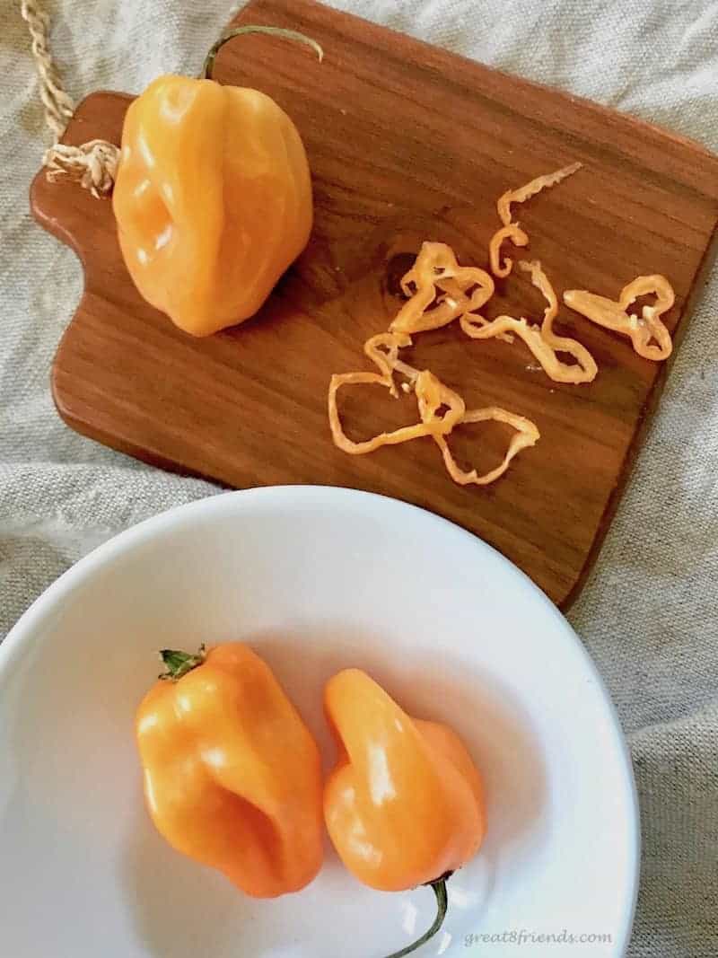 A whole and sliced scotch bonnet pepper on a wood cutting board.