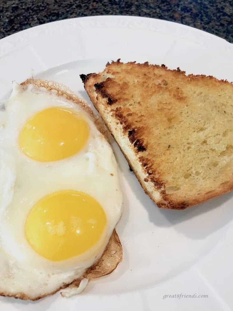 Toasted Onion Thyme Focaccia Bread with two fried eggs served on a white plate.