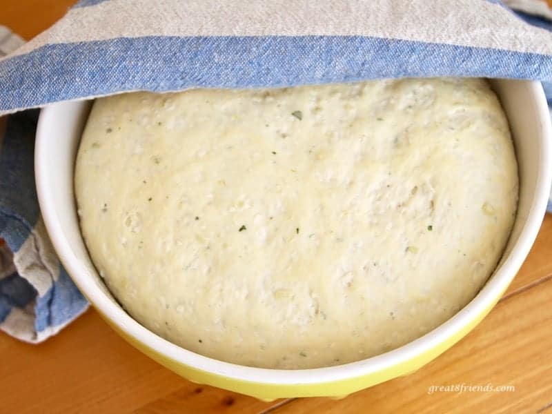 Rising Onion Thyme Focaccia Bread in a large bowl with a striped kitchen towel over half of the bowl.