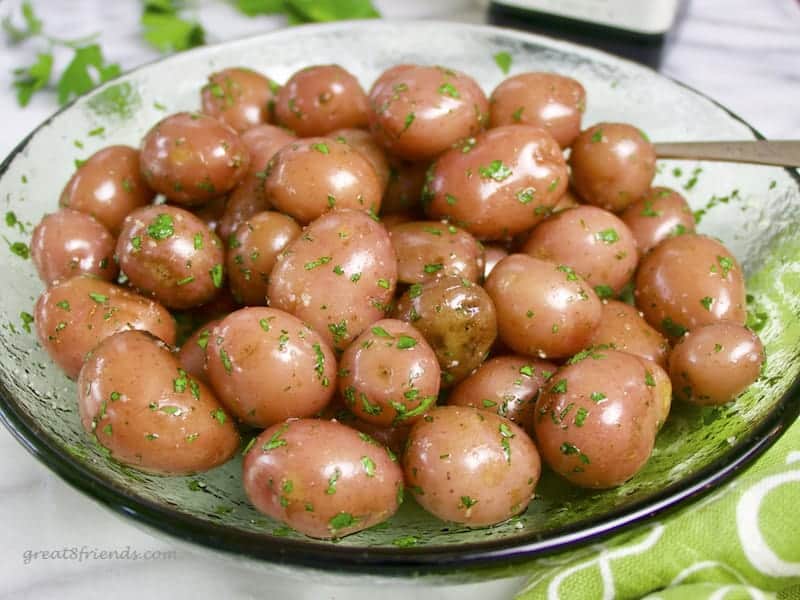 A green glass bowl of red new potatoes shiny with olive oil and sprinkled with salt and parsley.