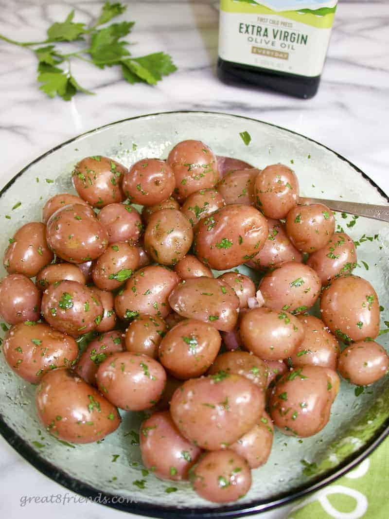 A green glass bowl of red new potatoes shiny with olive oil and sprinkled with salt and parsley.