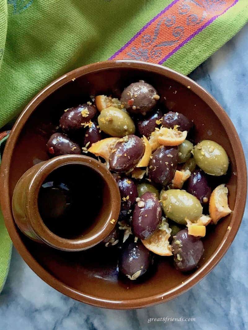 A brown pottery bowl filled with marinated olives.