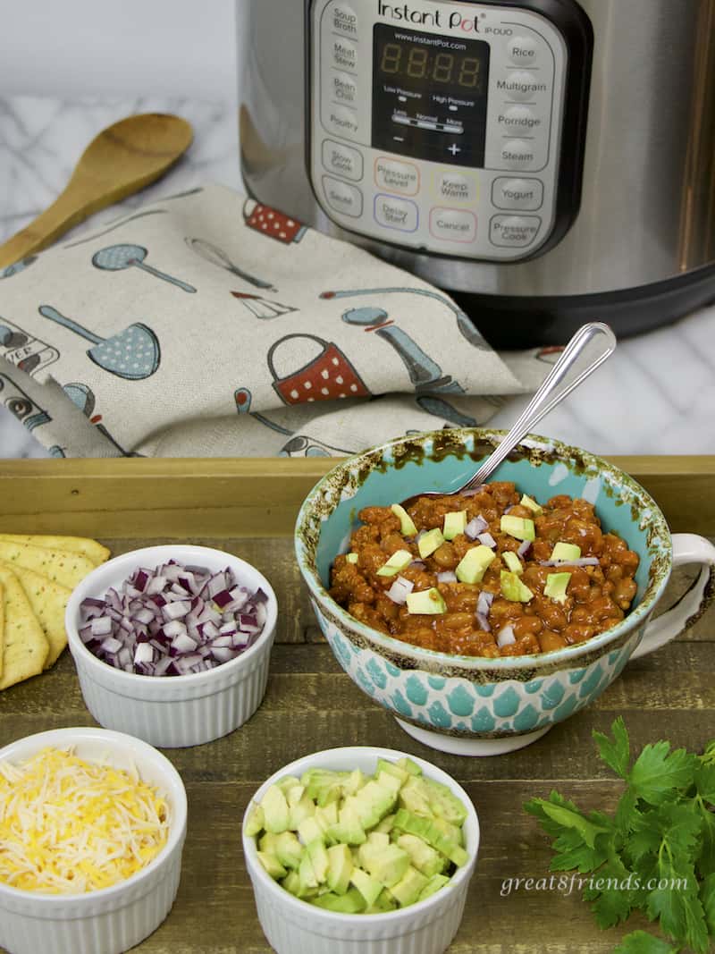 A large mug filled with chili surrounded by dishes of chopped onion, chopped avocado and shredded cheese. An Instant Pot in the background.