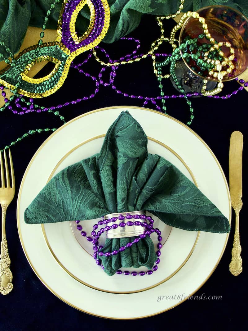 Mardi Gras place setting overhead shot with beads, china, gold flatware and fleur de lys napkin fold