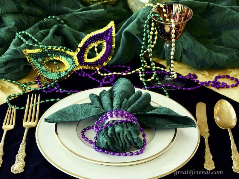 Mardi Gras Place Setting with beads, a mask and gold flatware.