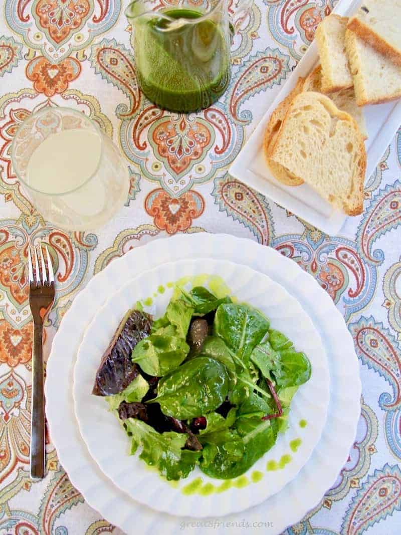 Green leaf salad with a arugula lemon salad dressing with some on the side in a glass pitcher.