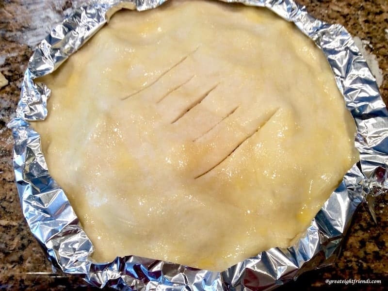 An apple pie before baking with the edge of the crust covered with foil.
