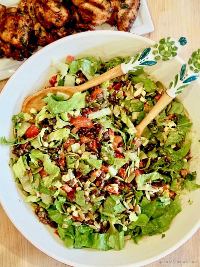 black bean salad in a large bowl with wooden tongs.