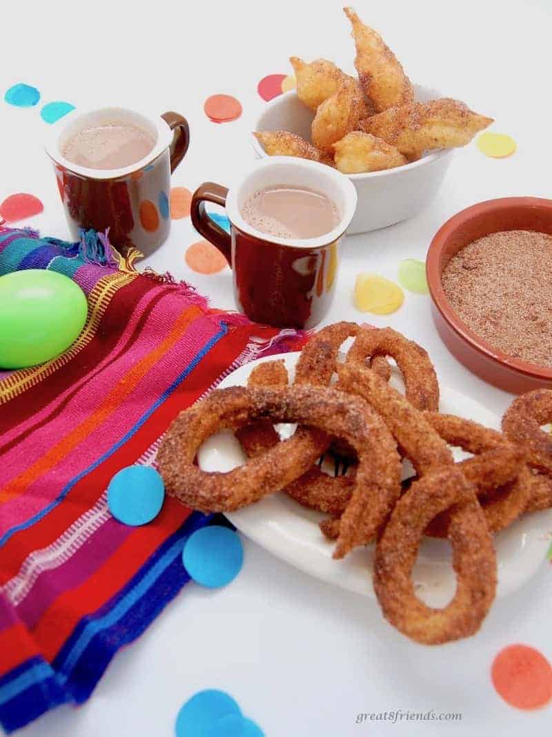 Curly churros with small cups of hot chocolate and a bowl of cinnamon sugar.