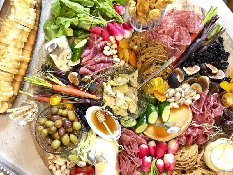 Overhead view of large round grazing board containing meats, cheese, fruits, veggies, crackers, breads, etc.