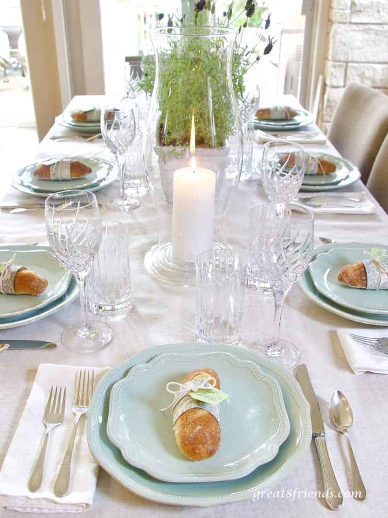 View of table for Provence dinner party, place settings, lit candle in hurricane and centerpiece.