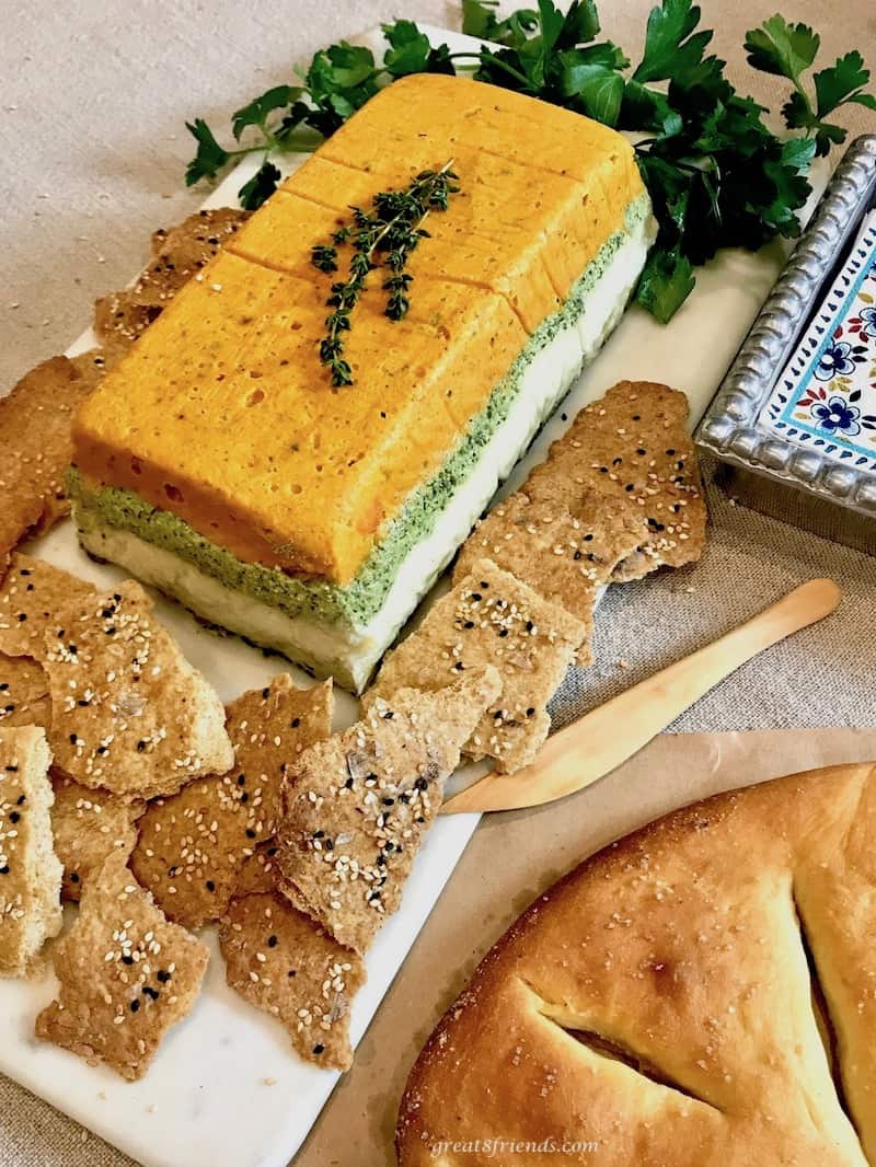 A layered vegetable pâté surrounded by crackers and parsley.