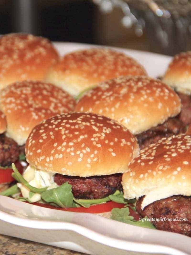 Several Cambozola beef sliders with Bacon Jam, arugula, sliced tomatoes on a sesame seed buns.