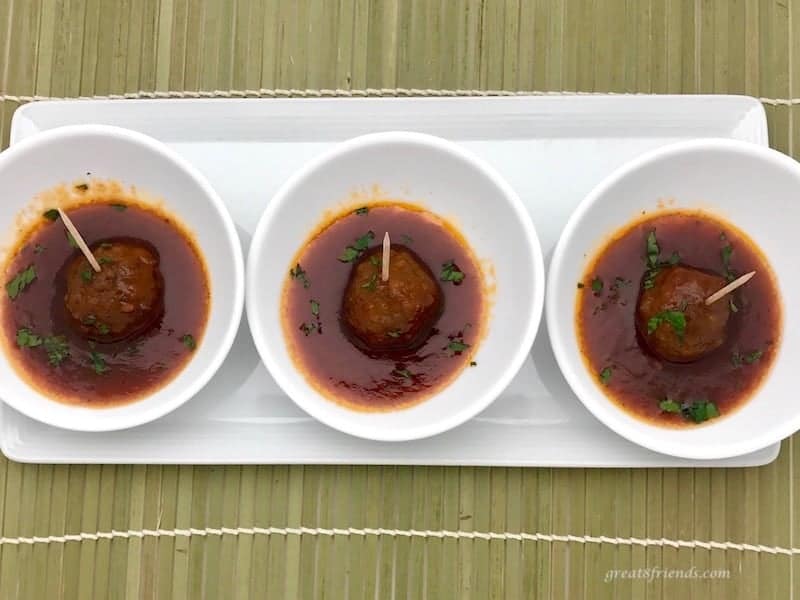 Three Hawaiian Meatballs each in it own small white bowl with sauce and a toothpick for eating.