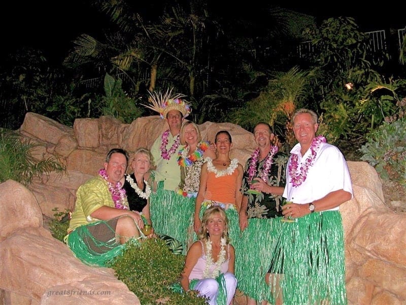 Eight people posing with grass skirts and leis on at a Luau dinner party.