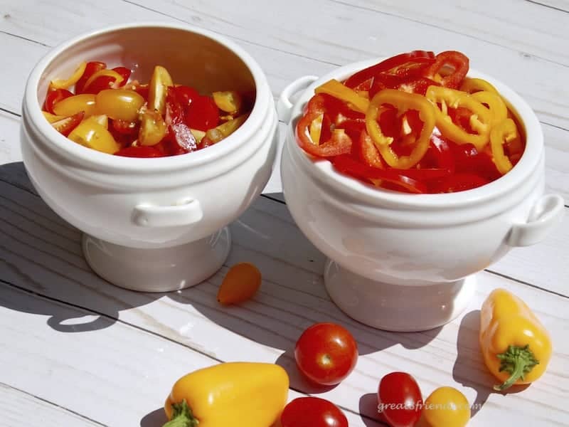 sliced pear tomatoes and sweet orange and yellow peppers in white bowls