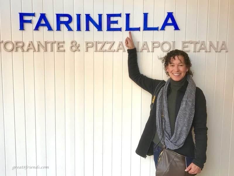A woman pointing to the word Farinella on a wall.