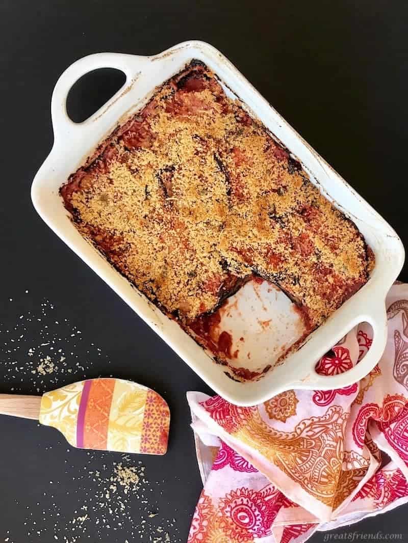 Large white baking dish of eggplant parmesan with one piece cut out. 