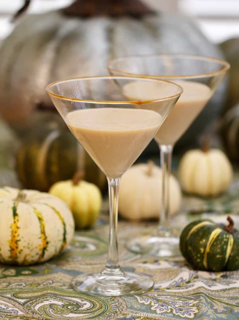 Two pumpkin martinis in stemmed martini glasses with small pumpkins surrounding.