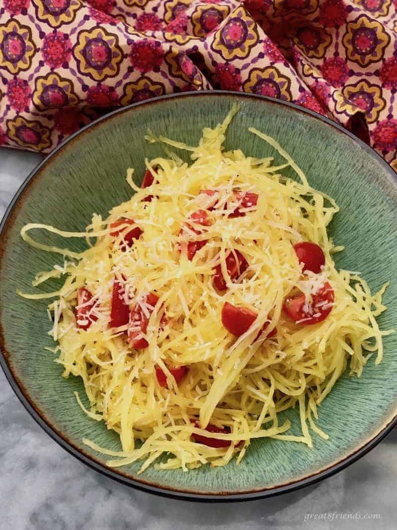 Bowl of spaghetti squash and tomatoes sprinkled with cheese.