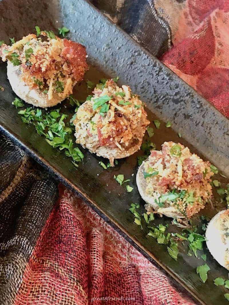 Individual mushrooms stuffed with prosciutto and parmesan served on a rectangular platter as an appetizer.