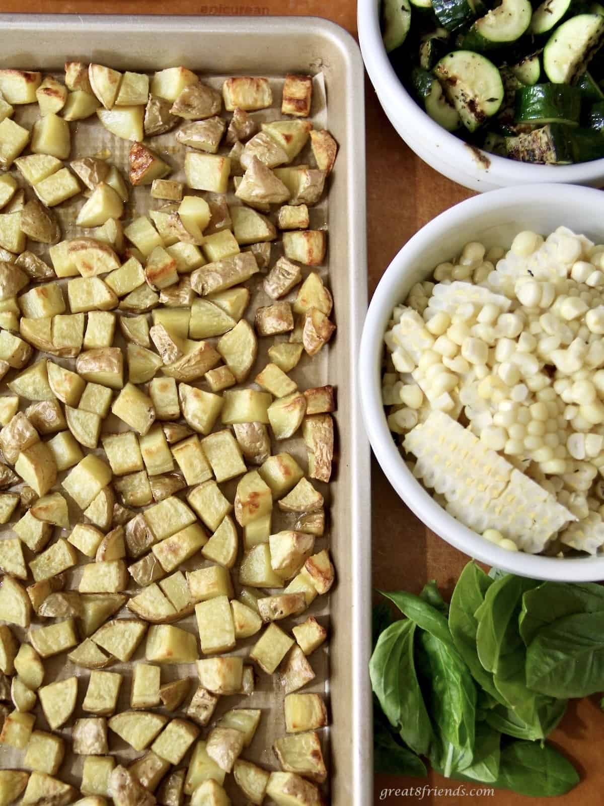 Diced roasted potatoes, grilled zucchini, grilled corn and basil laid out and ready to be combined in a salad bowl.