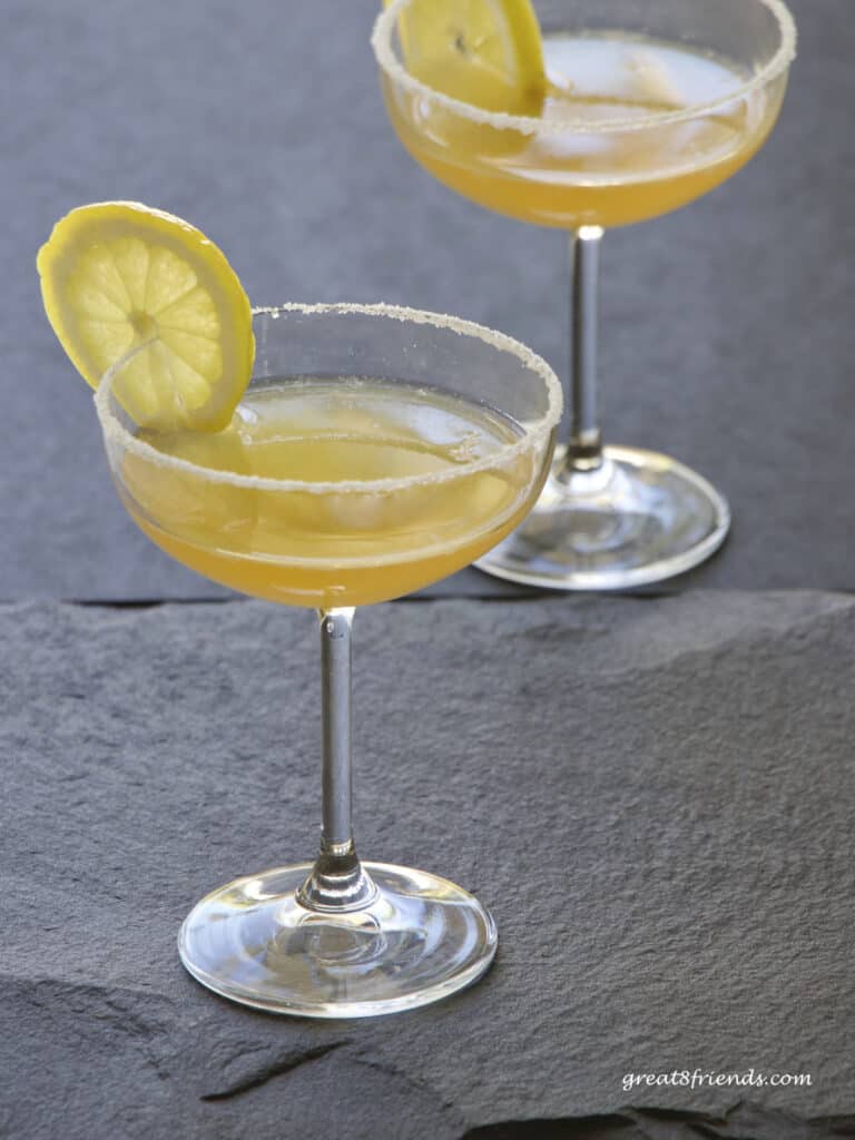 Two sidecar cocktails in coupe glasses garnished with lemon slices.