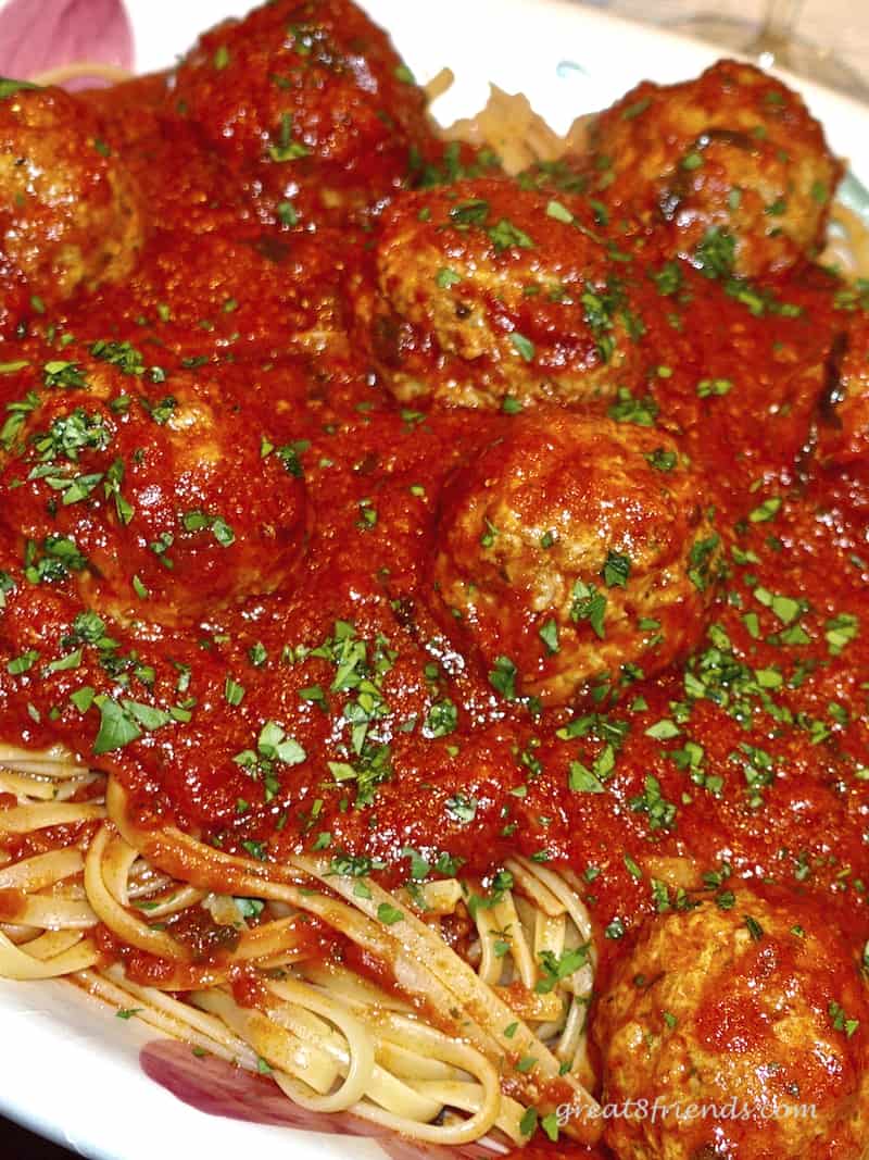 CloseUp vertical photos of spaghetti and meatballs garnished with chopped parsley.