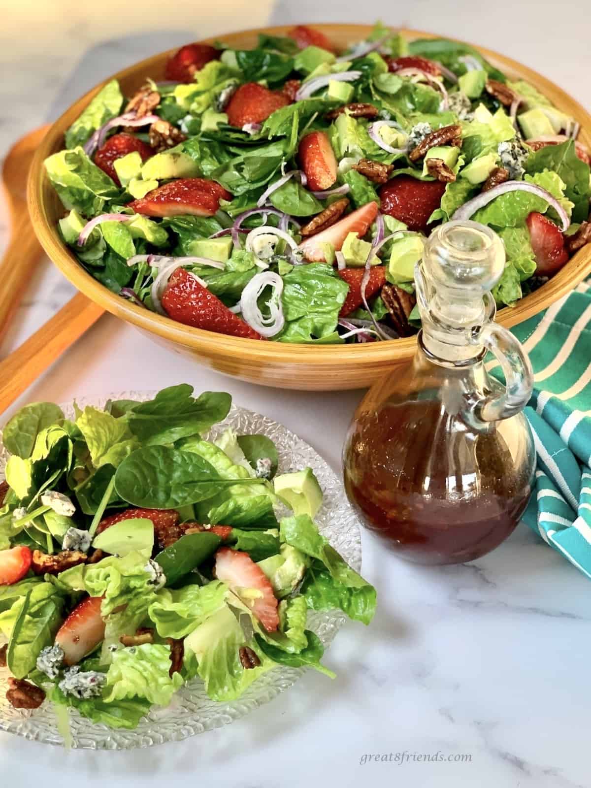 A plate of salad with a cruet of dressing and a large bowl of salad in the background.