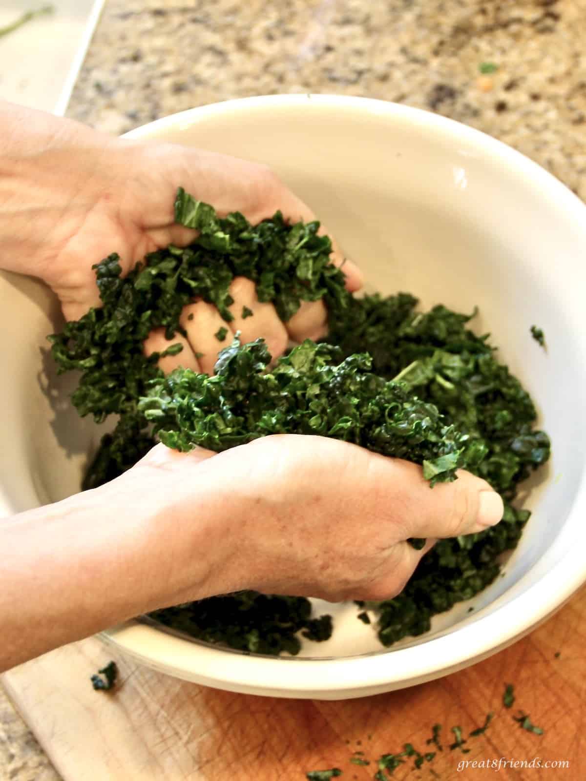 A bowl of torn tuscan kale leaves that are being massaged with someones hands.