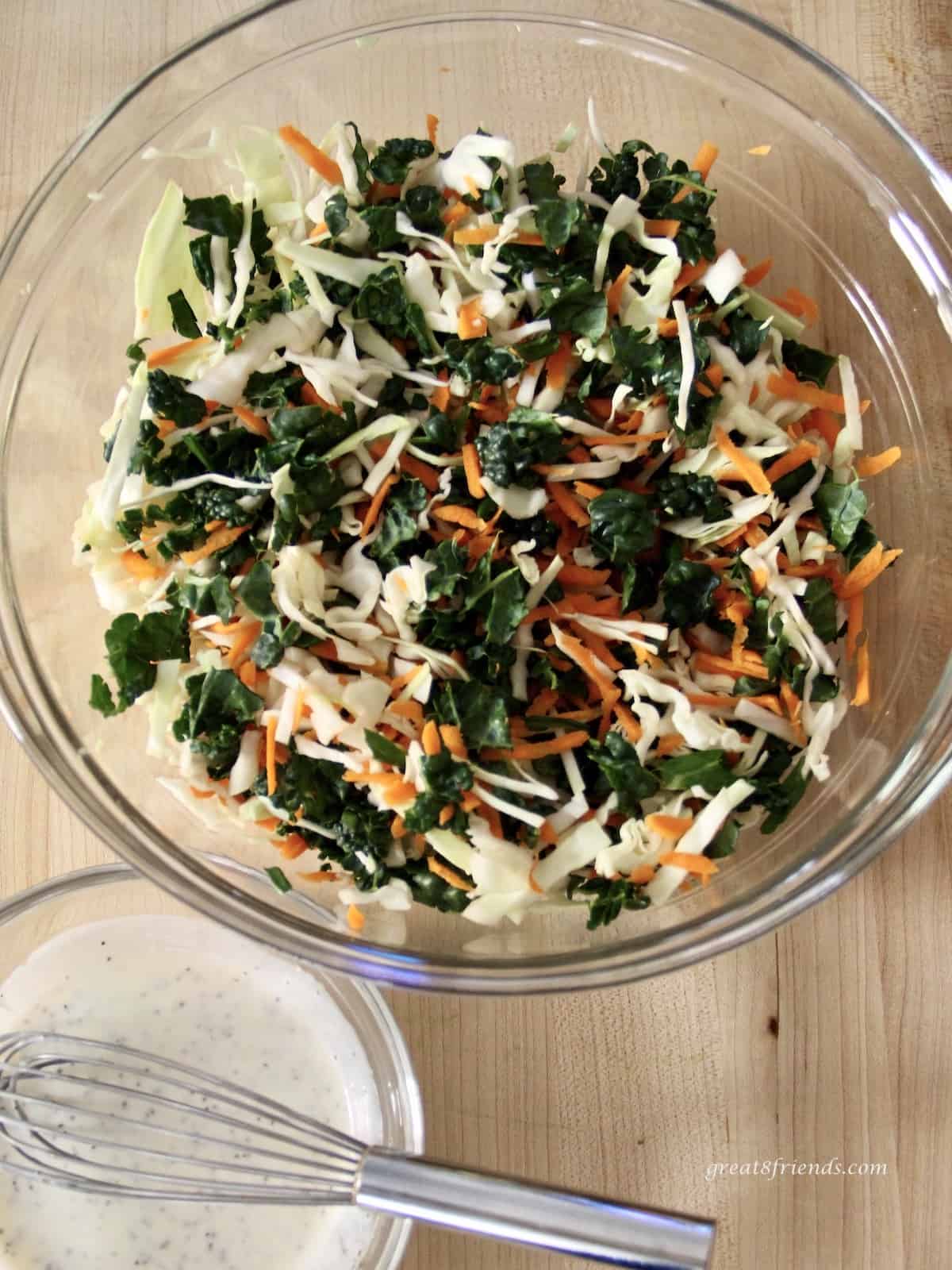 A coleslaw salad including cabbage, kale and carrots with a dressing for the slaw on the side.